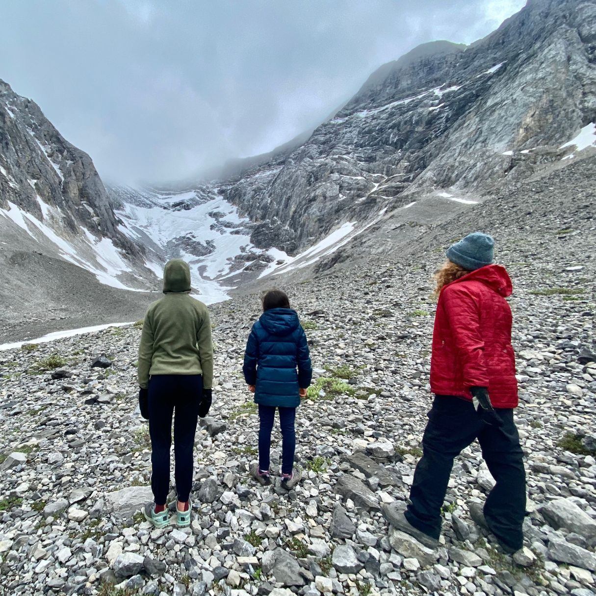 Hikers stand on a rocky trail overlooking a glacial valley and mountainside streams.