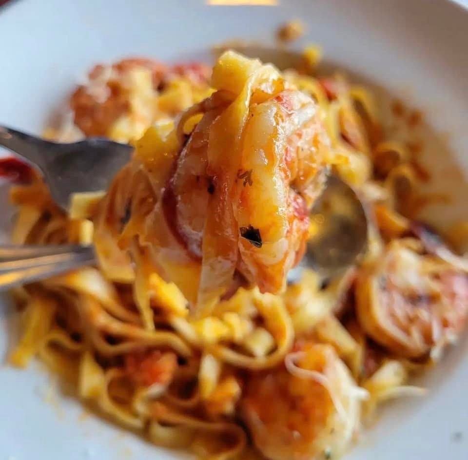 Fork lifting a bite of pasta coated in rich sauce with sausage and melted cheese in a white bowl.