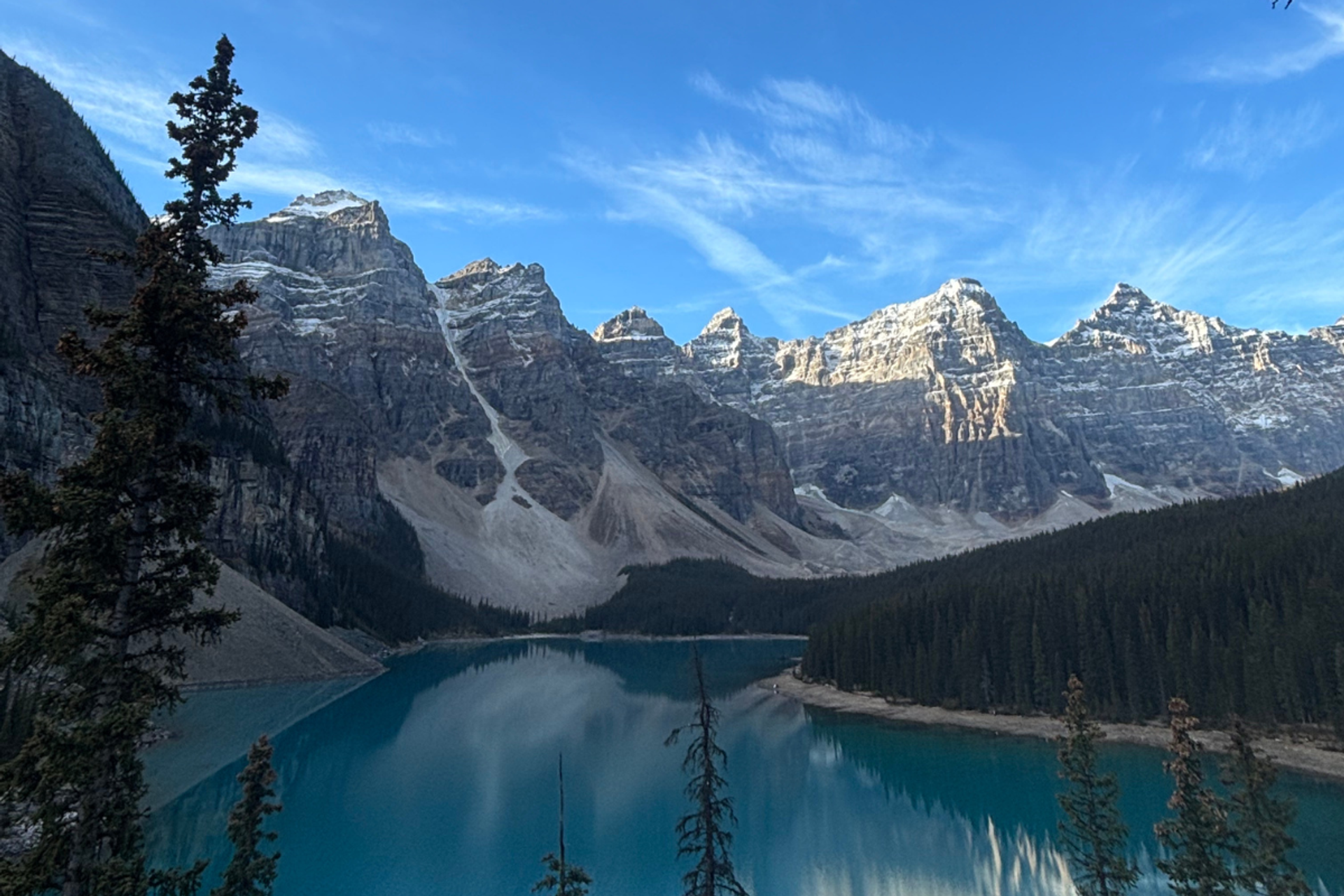 Turquoise lake surrounded by pine trees and towering rocky mountains under a clear blue sky.