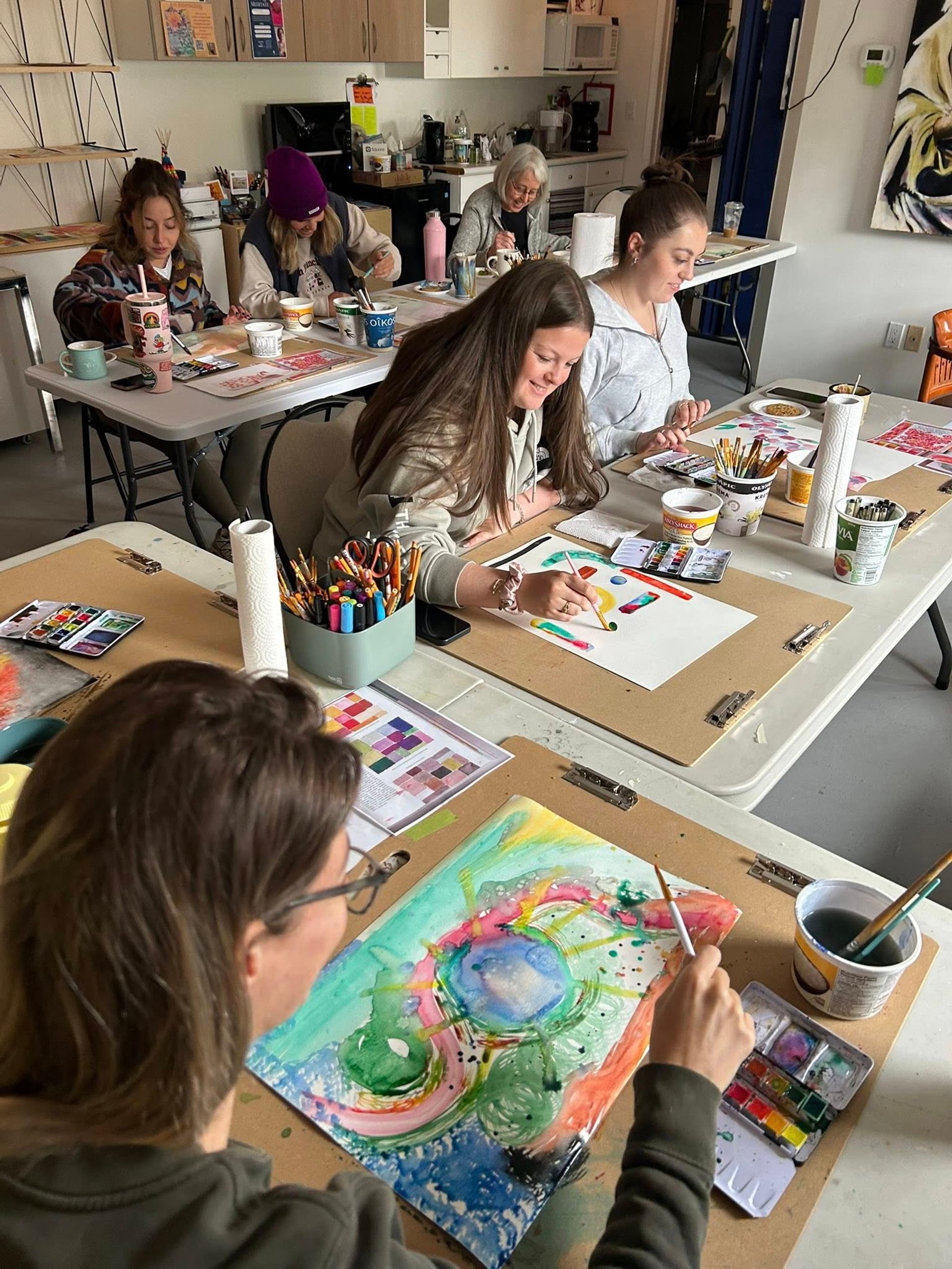 Group painting in art classroom with colorful supplies and abstract artwork.