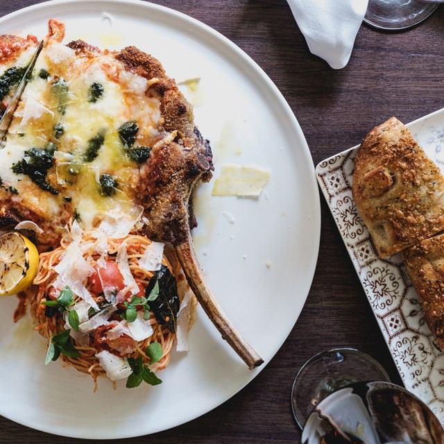 Plate with cheesy meat dish and pasta served alongside crusty bread on a wooden table