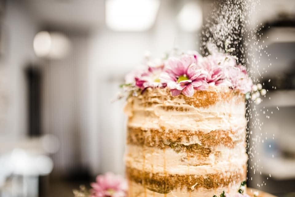 Layered naked cake topped with pink flowers and powdered sugar