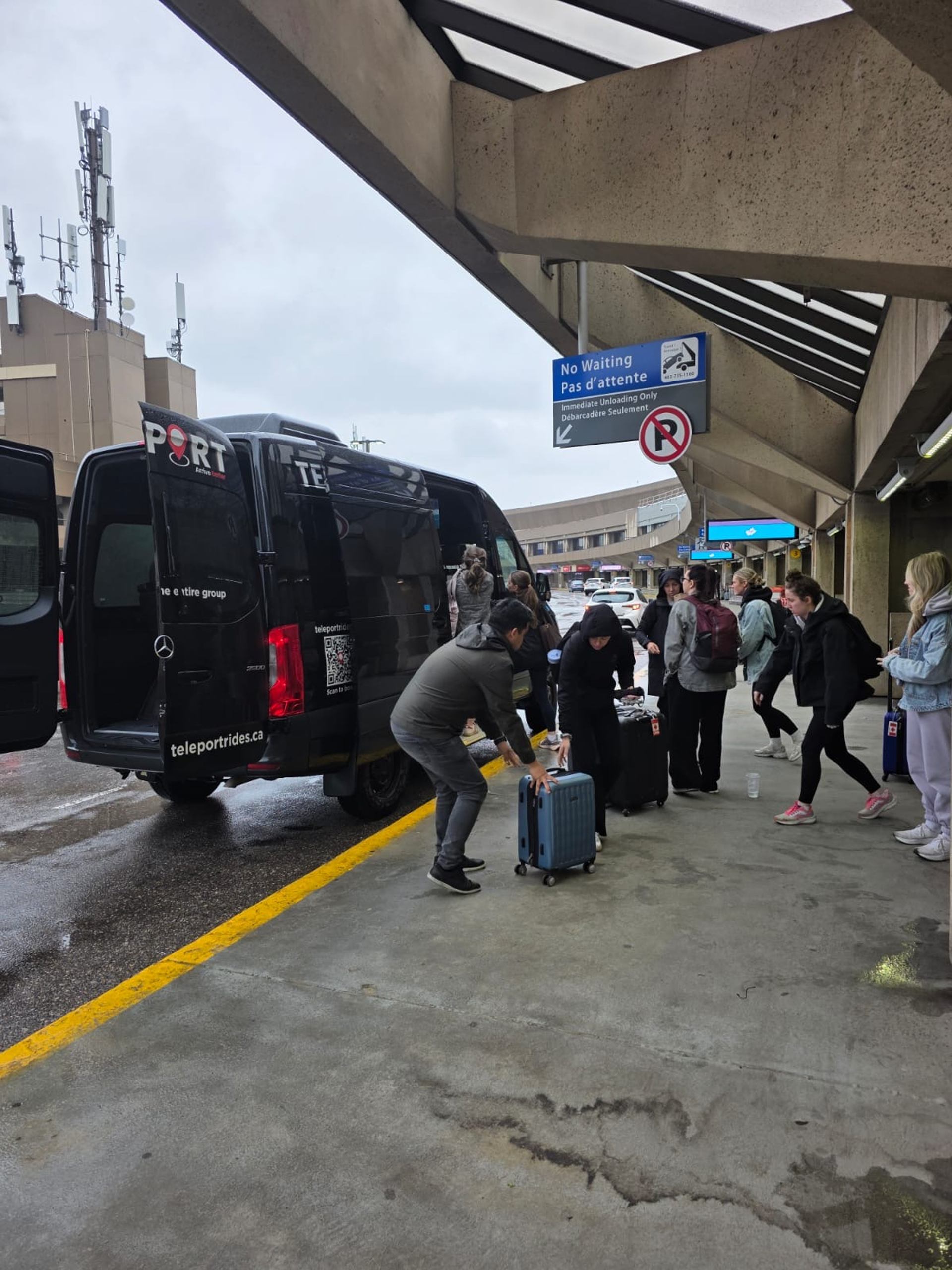Travellers unload suitcases from a Teleport shuttle van at airport curbside.