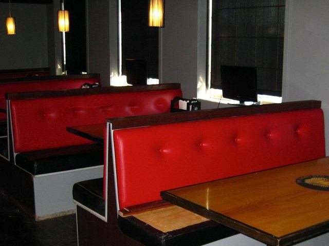 Red booth seating and wooden tables inside a pub with wall lamps and dark flooring.