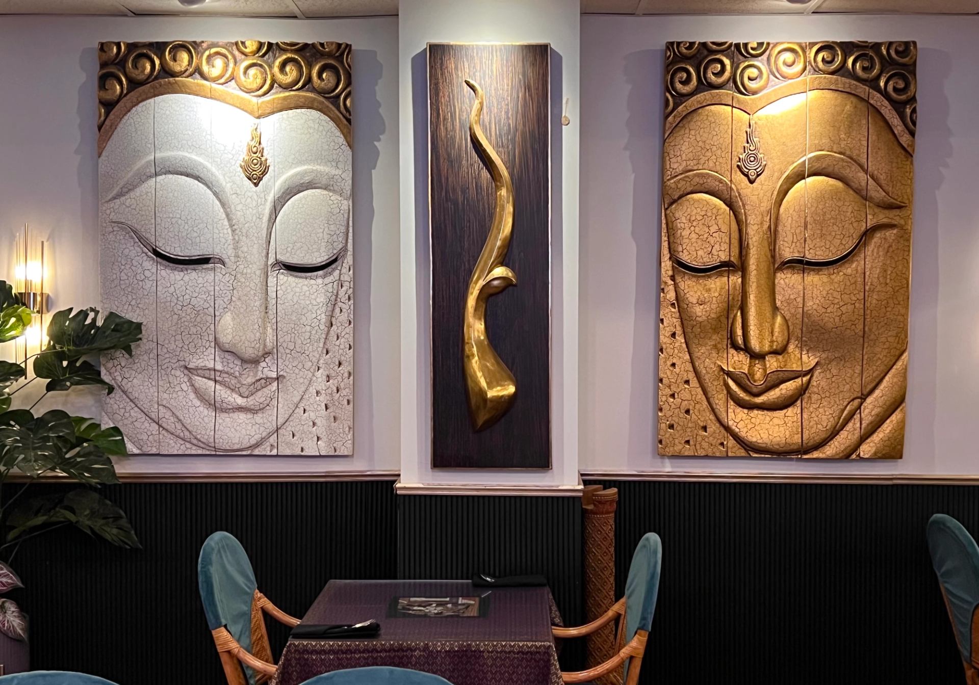 Restaurant wall with large Buddha face artworks above table and teal upholstered chairs.