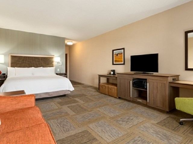 Modern Hampton Inn room with king bed, TV, desk, and cozy seating area.