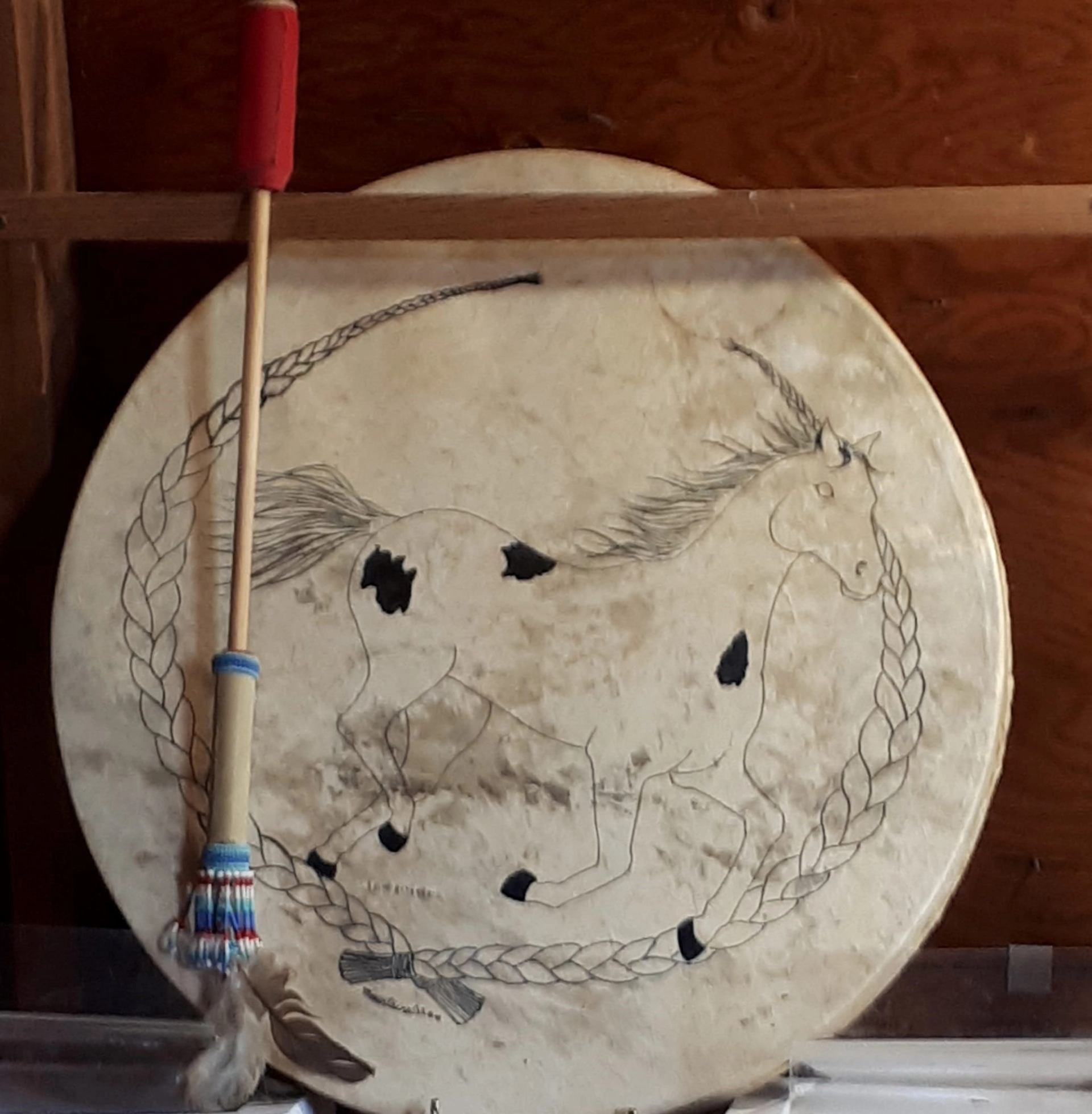 White decorative drum with painted horse and rope border, displayed indoors.