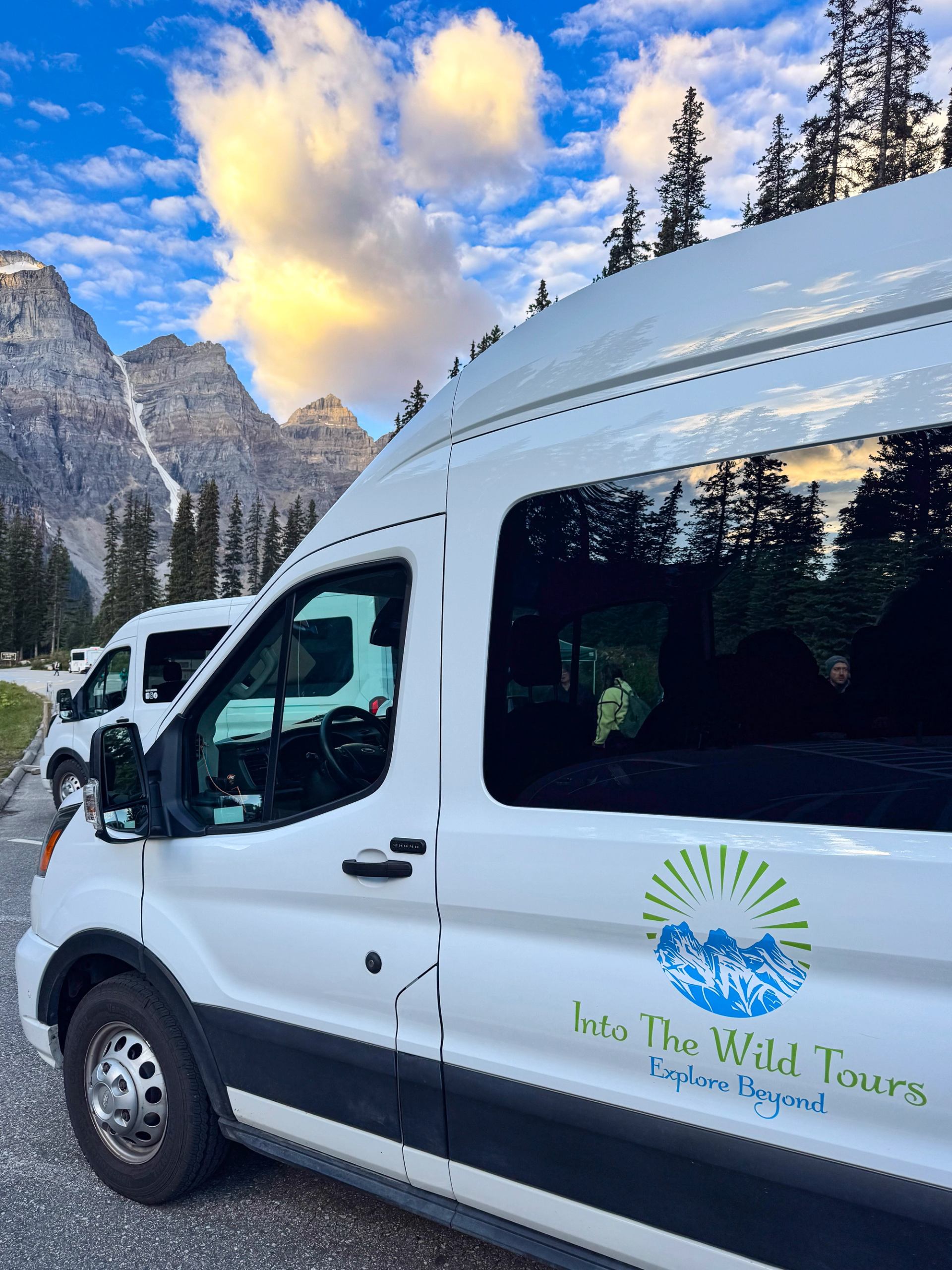 Into the Wild Tours van parked below mountain peaks and sunrise clouds.