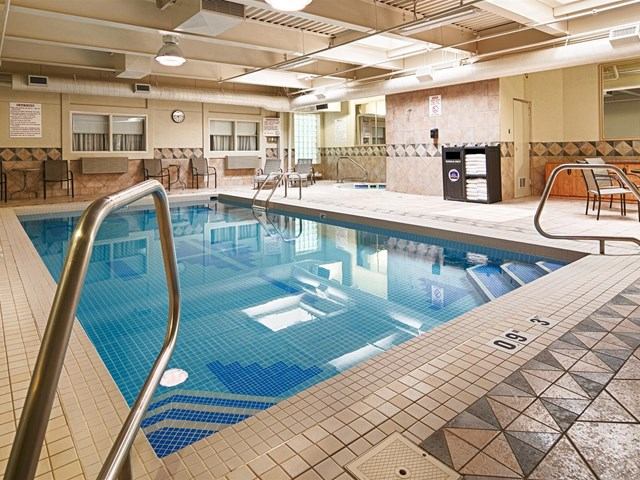 Indoor pool area with tiled deck, clear water, and seating along the sides.