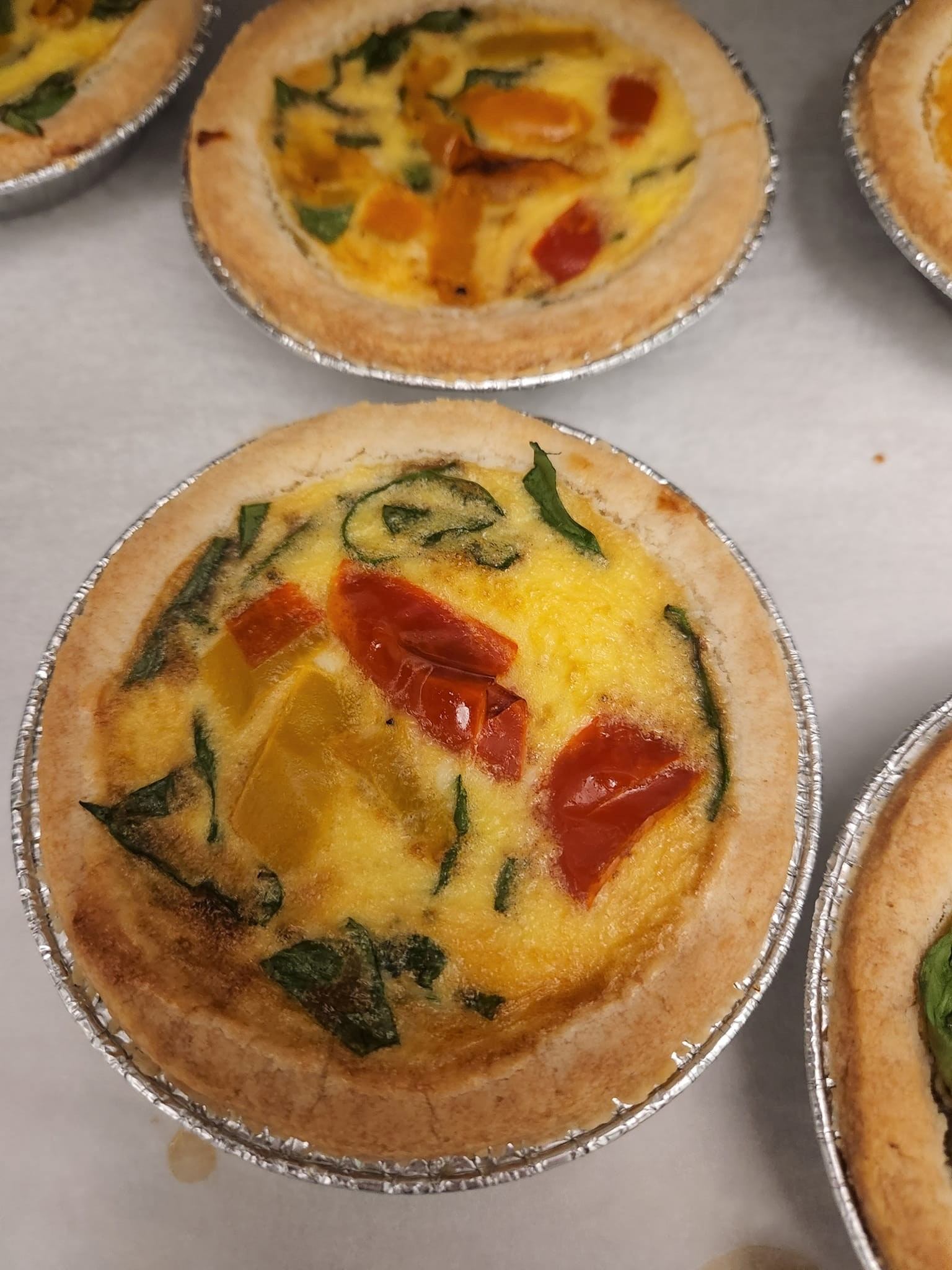 mini pizzas on foil trays, topped with spinach, peppers, and melted cheese.