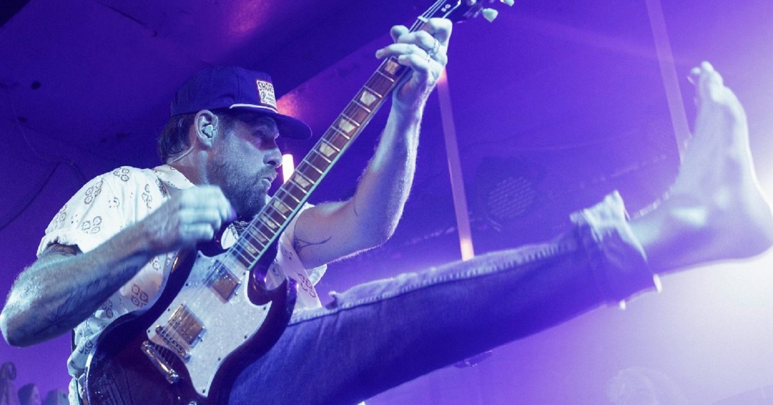 Guitarist mid-jump on stage with purple lights in the background.