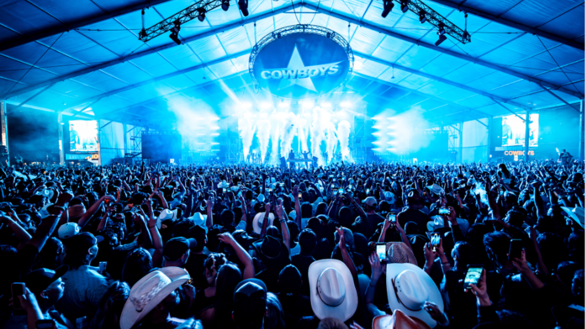 Large crowd facing a brightly lit concert stage inside a festival tent at Cowboys Music Festival.