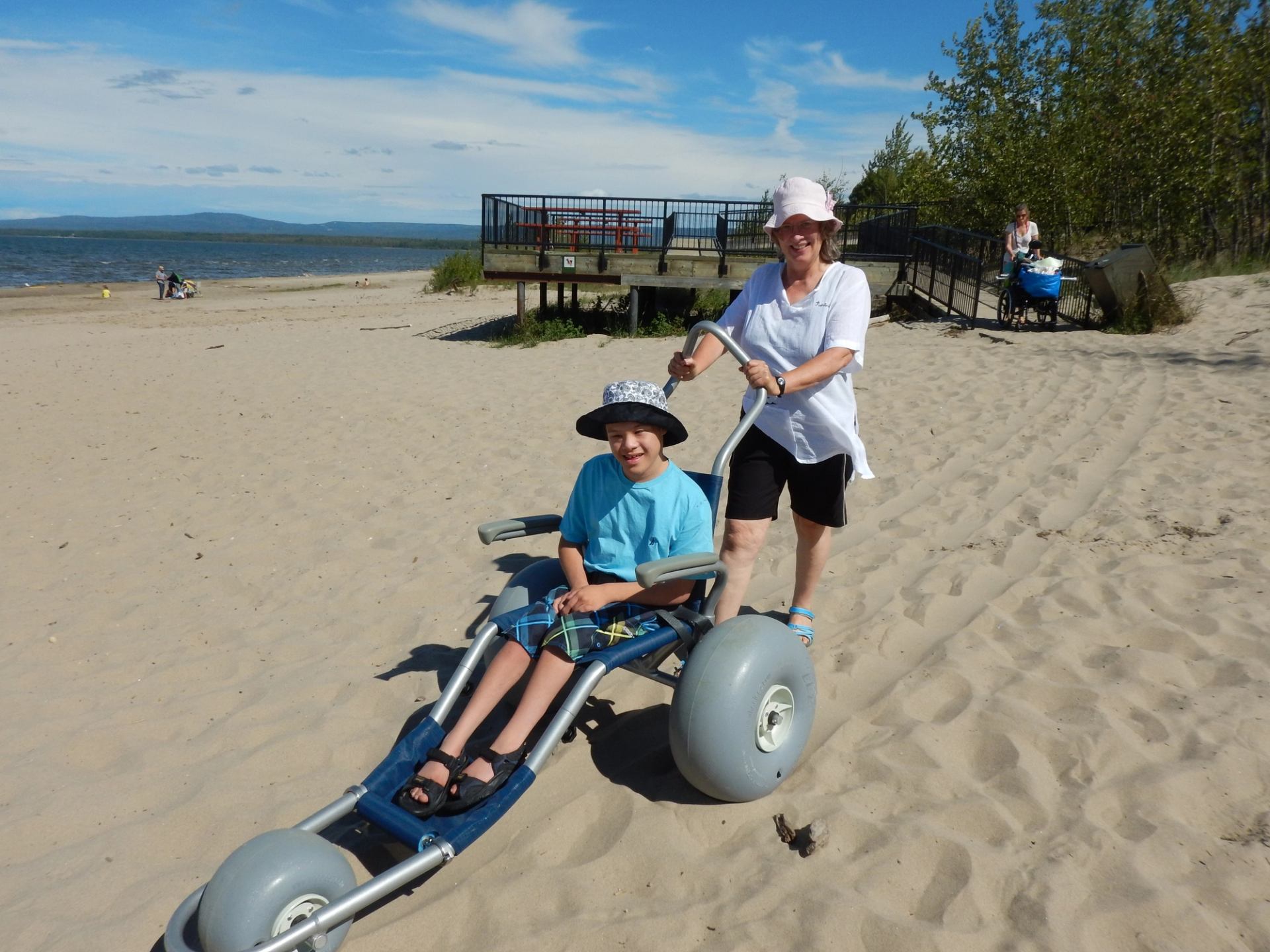 A woman pushes a young man in a wheelchair on a beach.