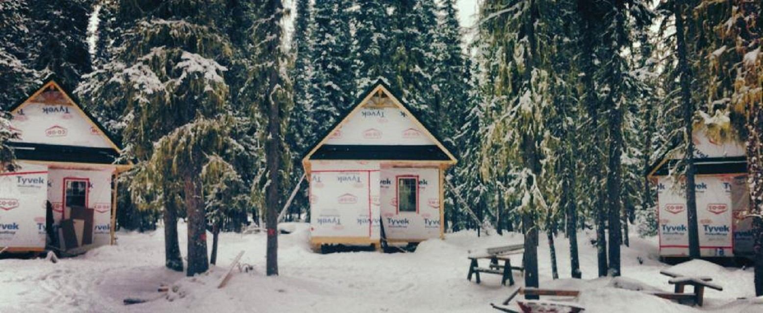Small cabins surrounded by snow and evergreen trees at Frontier Lodge in winter.