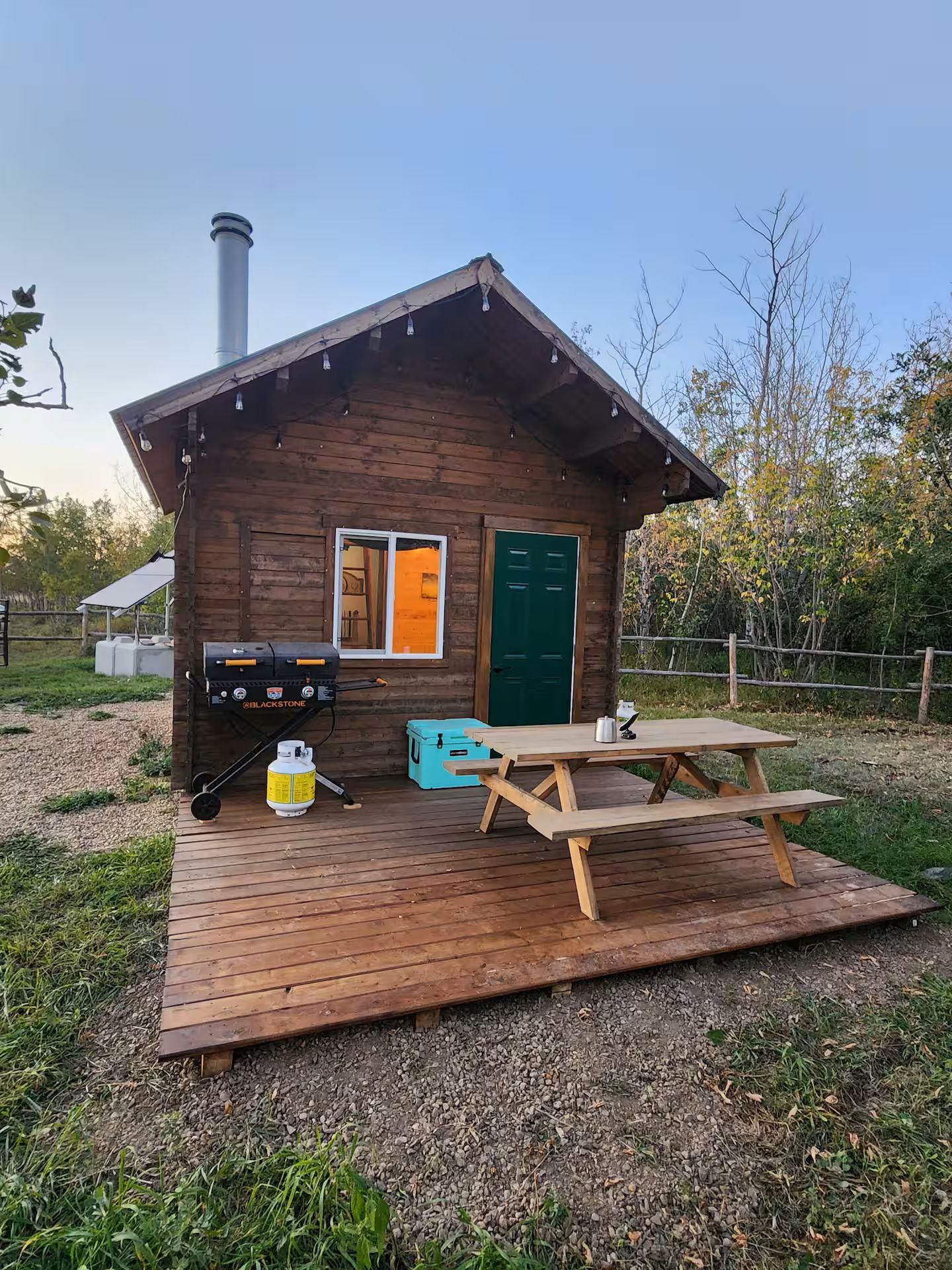 Small wooden cabin with a deck, picnic table, and grill in a grassy yard.