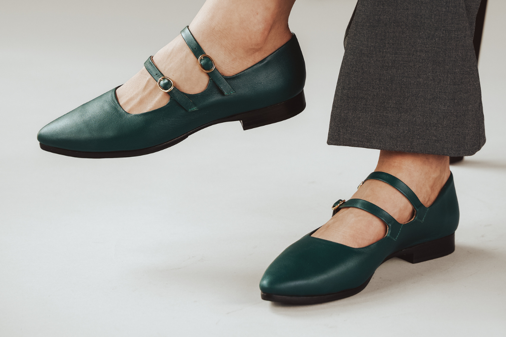 Green Mary Jane shoes with double straps, worn with gray pants.