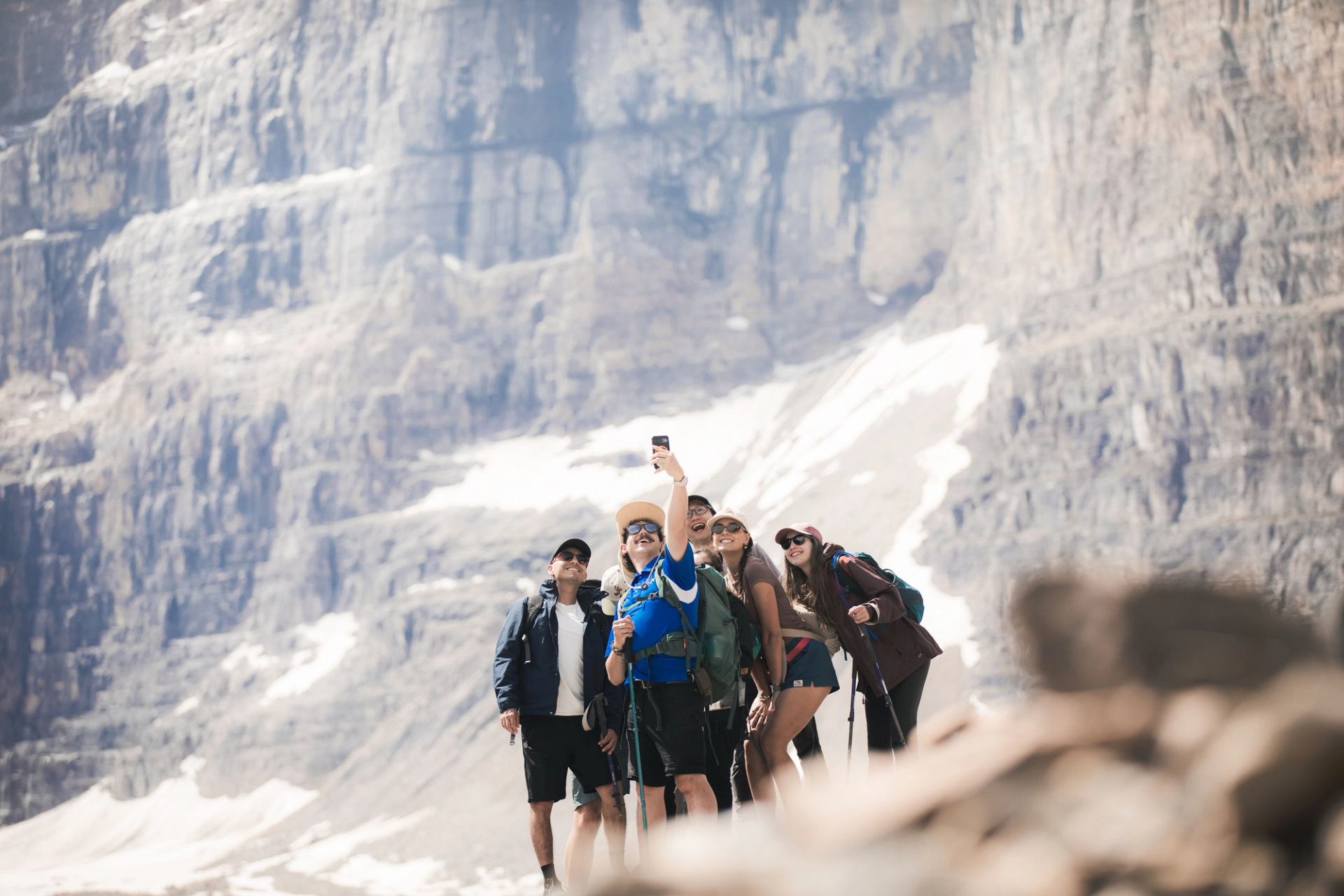 Group of hikers take a selfie on rocky mountain trail with snow patches.