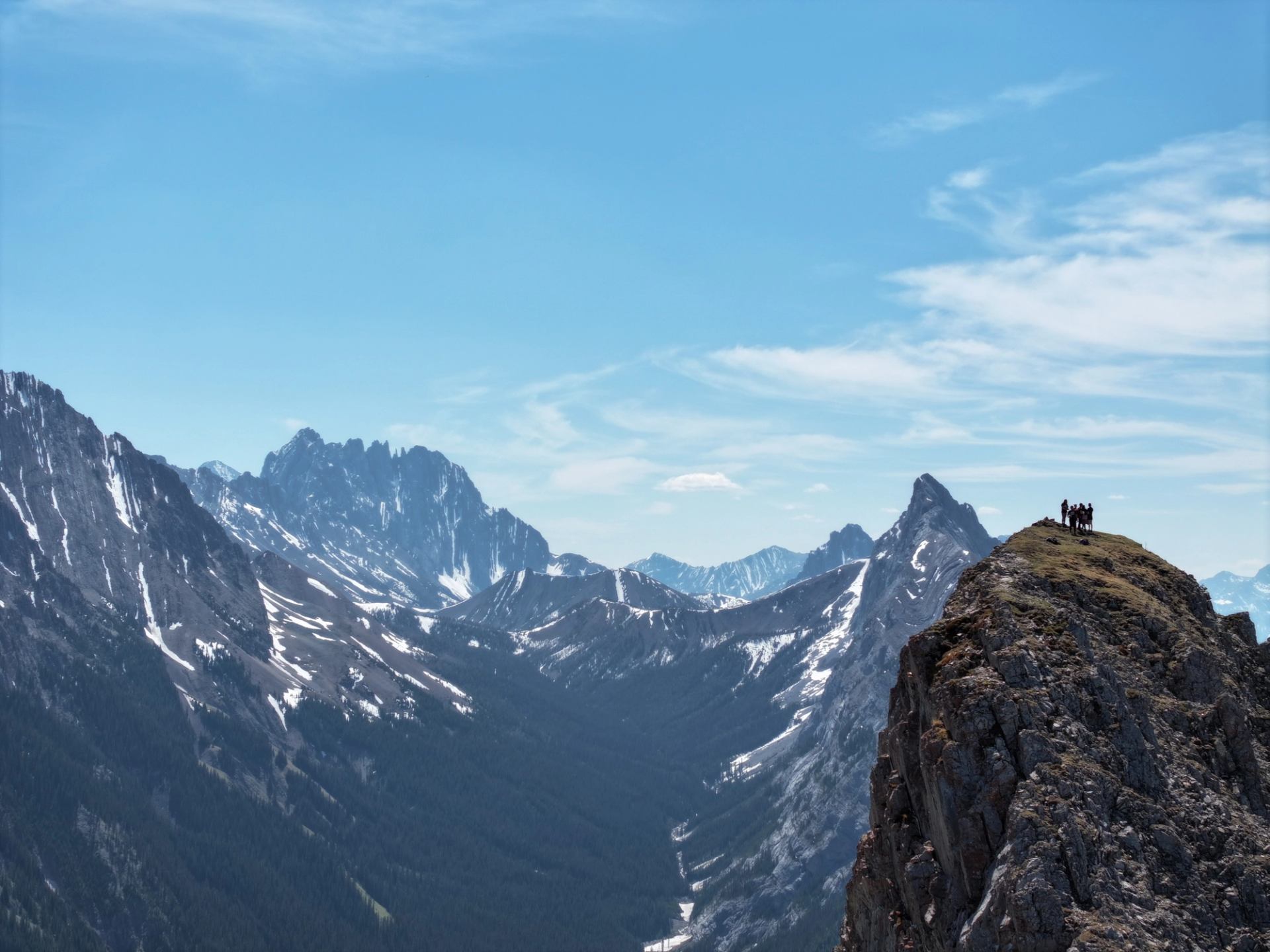 Two people on cliff with snowy mountain peaks in background.