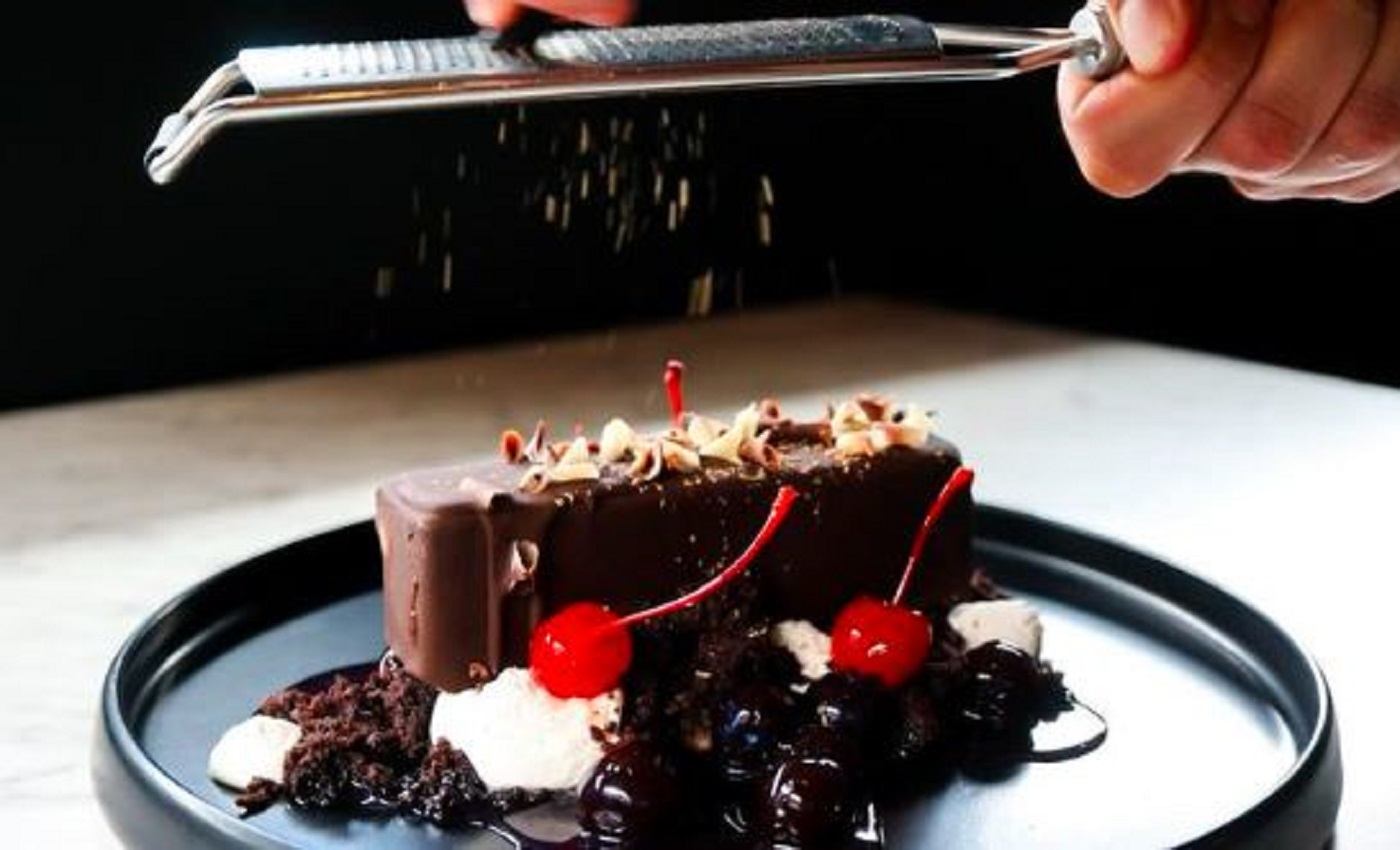 Garnish being grated onto a chocolate dessert with cherries.