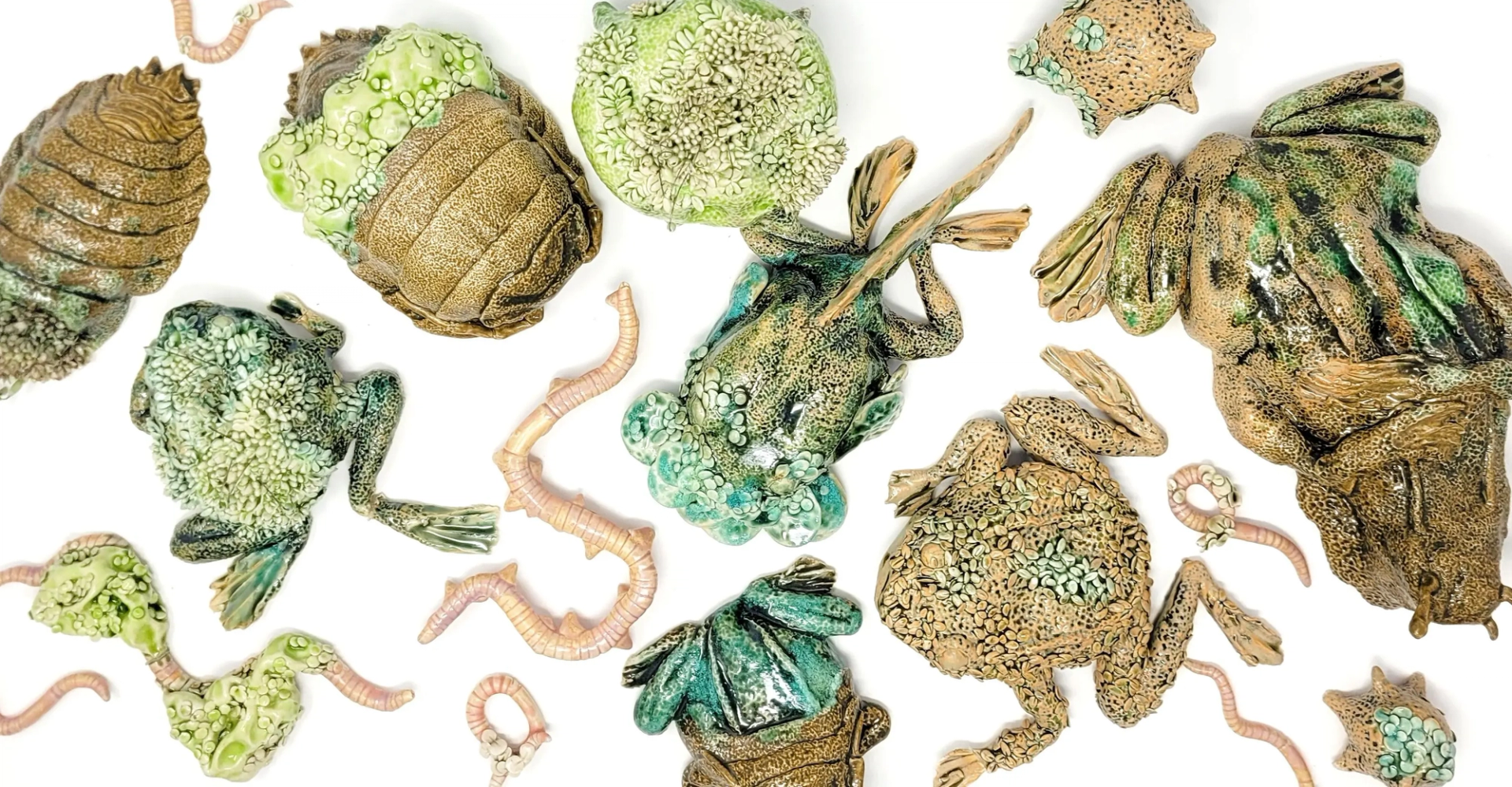 Ceramic frogs and segmented worms arranged on a white background in scattered positions.