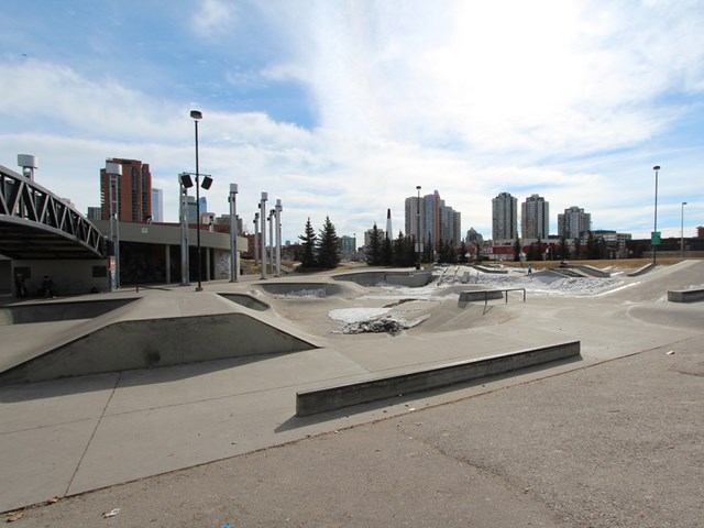 Concrete skatepark with ramps and rails, Calgary skyline in the background.