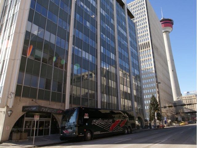 Black Red Arrow Motorcoach in front of urban tower.