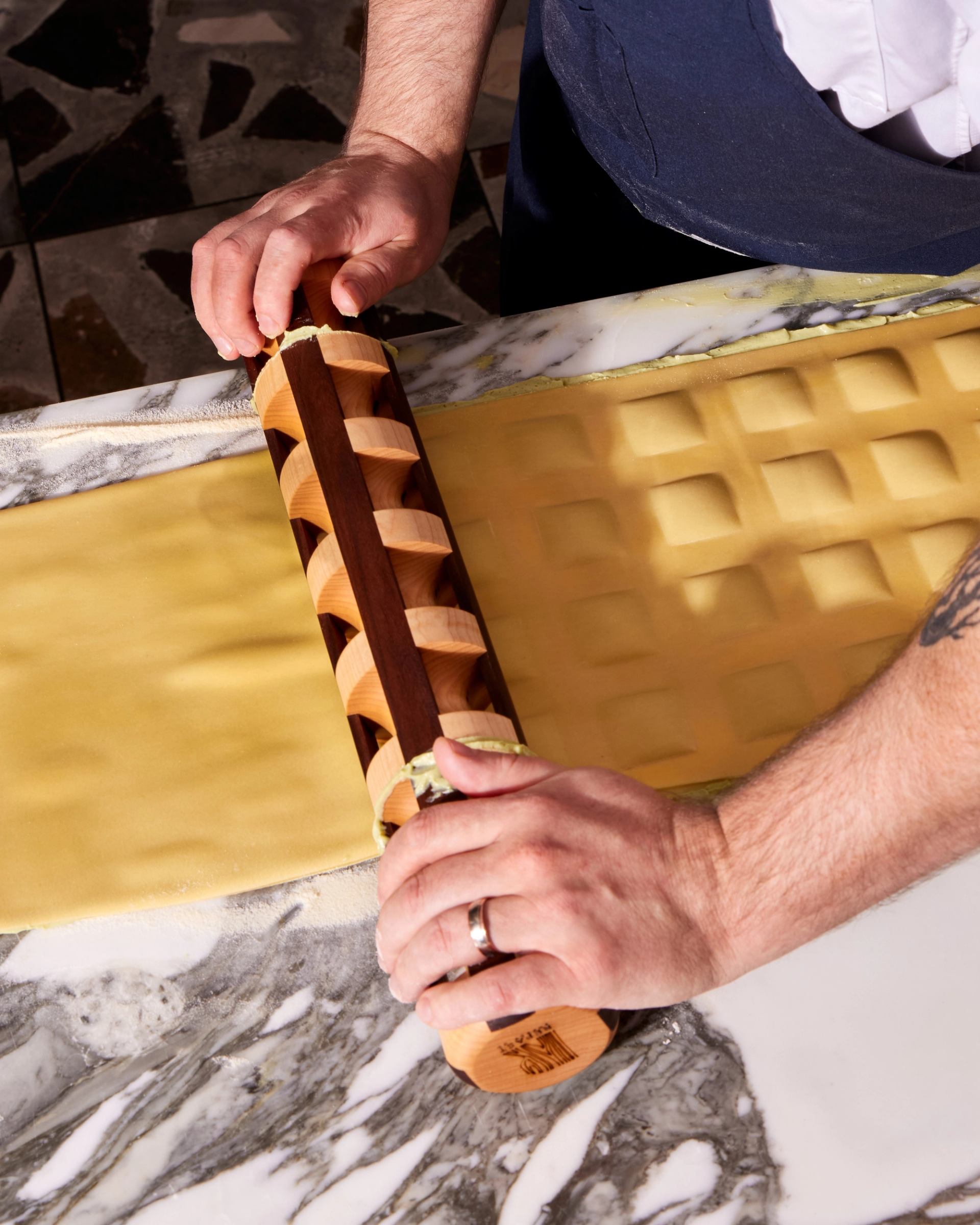 Hands assemble a wooden slat pizza box with a marble tabletop in view.