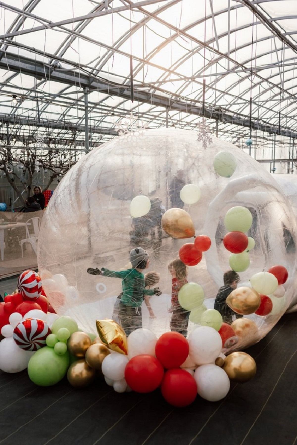 Kids playing in festive balloon-filled dome at indoor Christmas market.