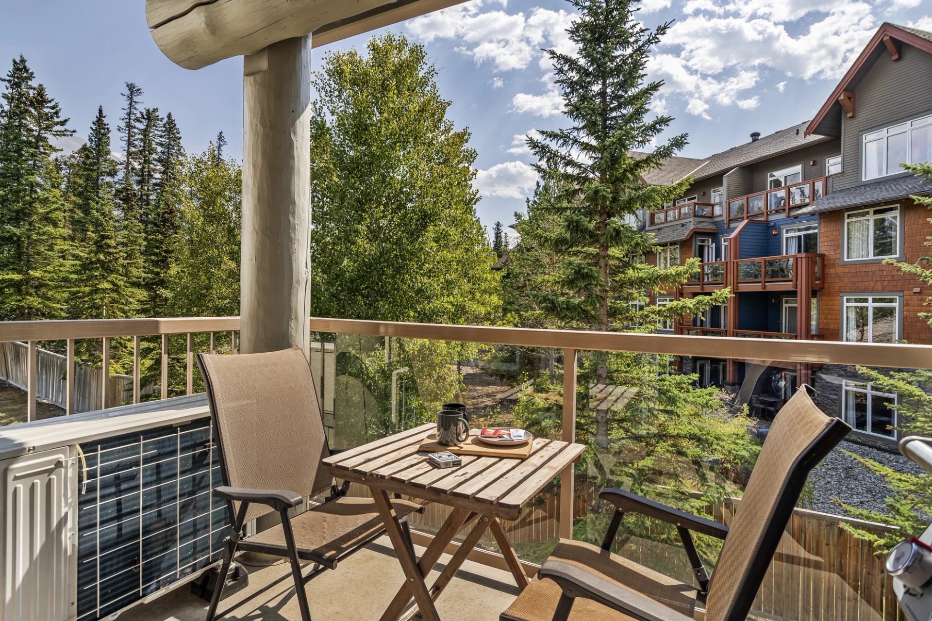 Balcony with two chairs and a table overlooks trees and neighbouring homes.