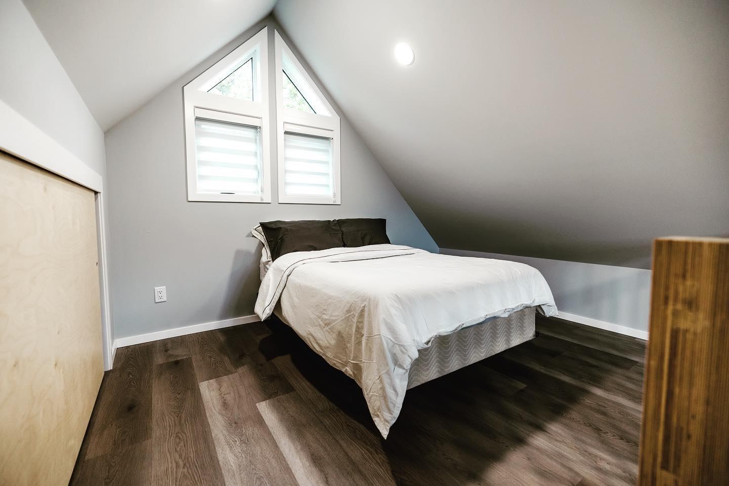 Loft bedroom with a double bed, sloped ceiling, and bright triangular window.