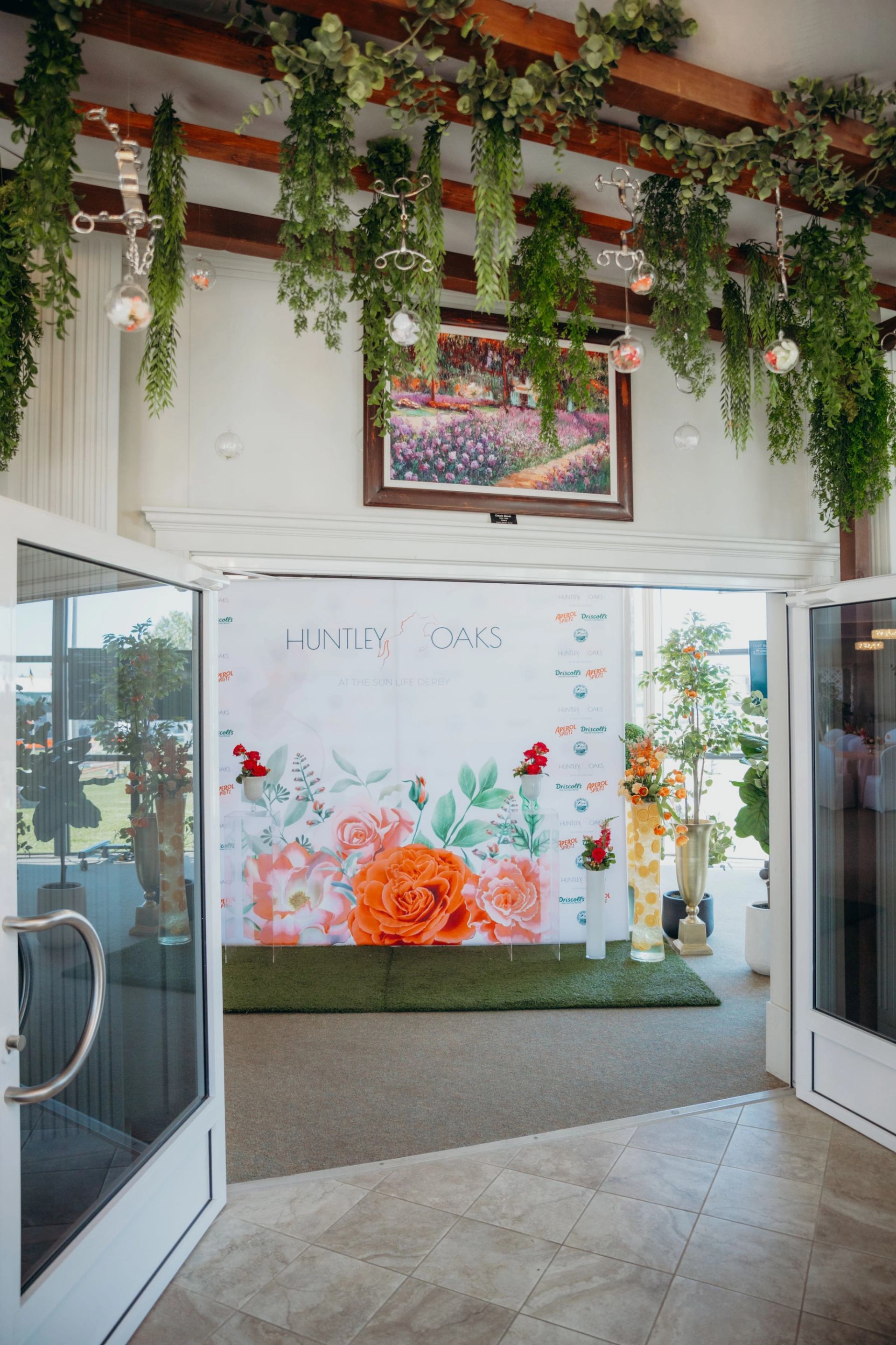 “G” Huntley Oaks event banner under hanging greenery and hanging glass lights, indoors.