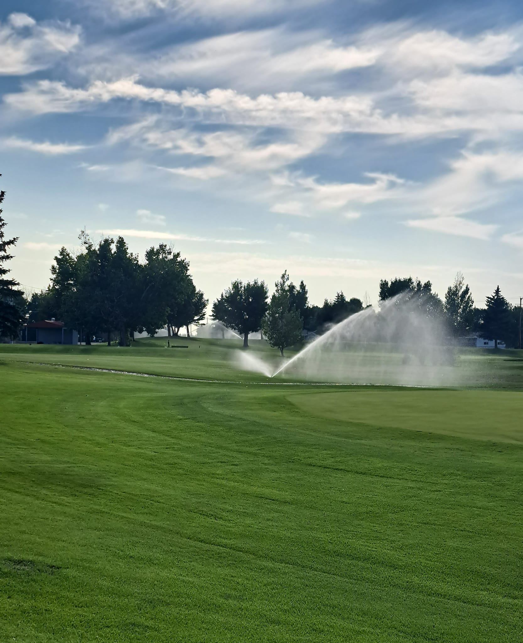 Sprinklers watering a bright green fairway under a partly cloudy sky.