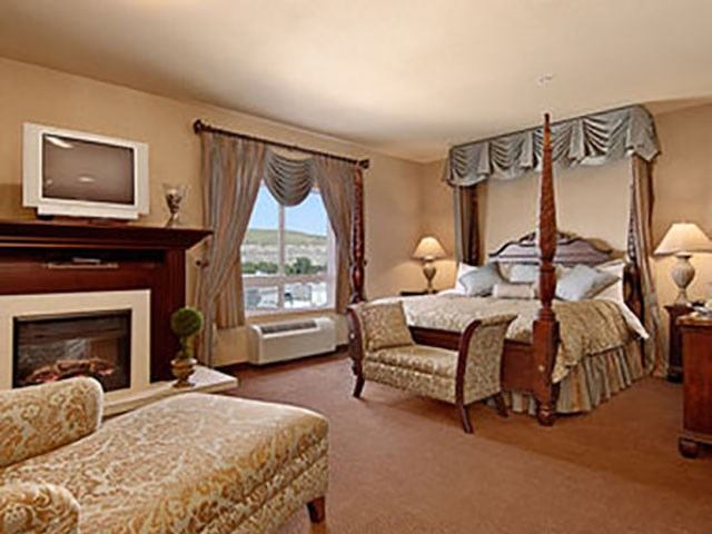 Elegant hotel suite with a four-poster bed, fireplace, chaise lounge, and classic décor.