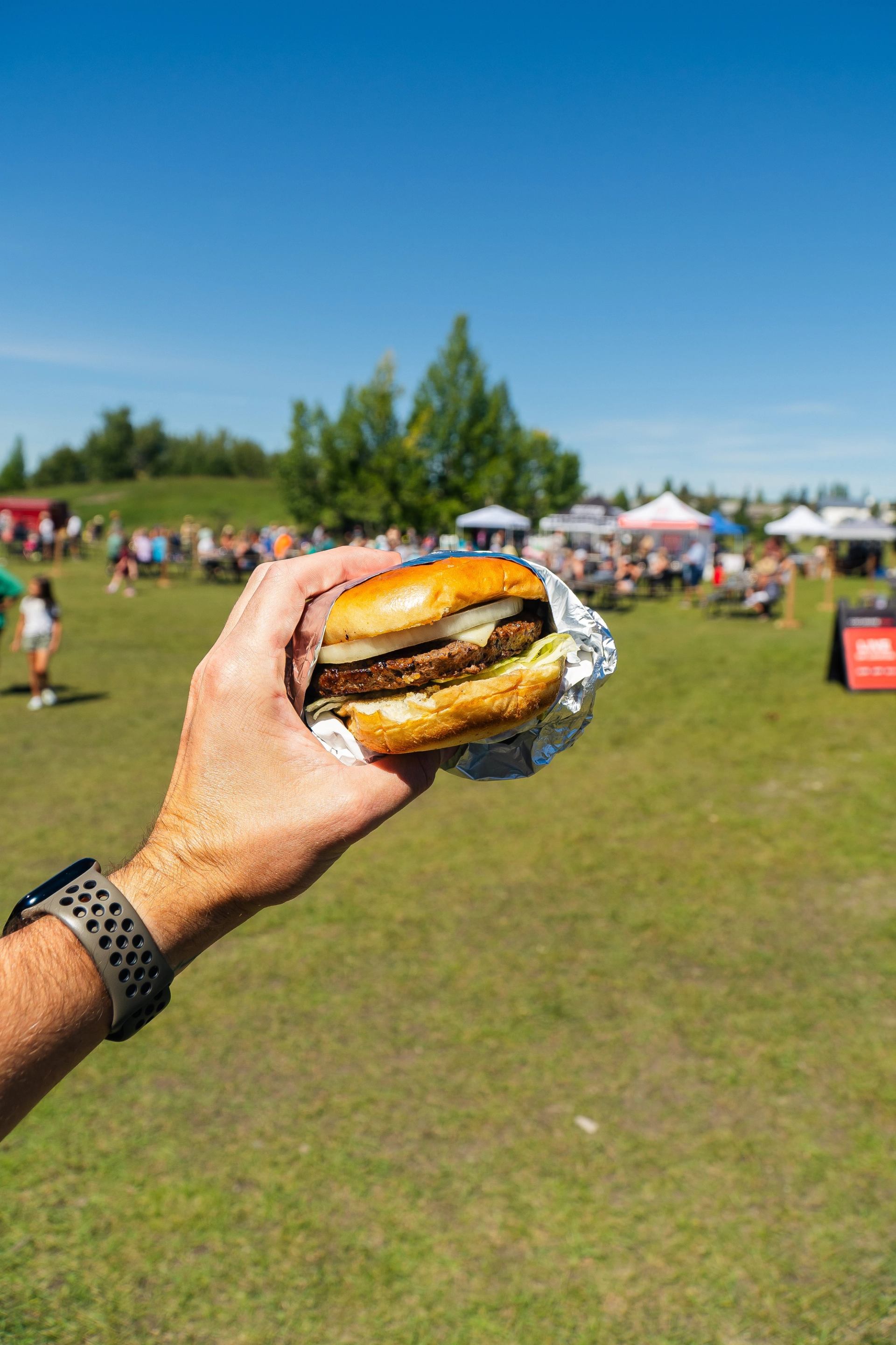 A person holding a burger with food trucks in the background.