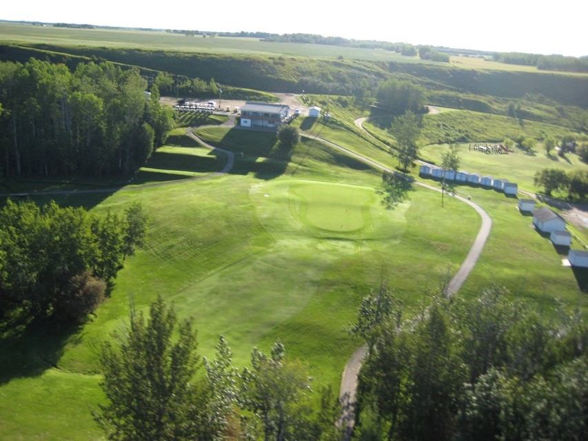 Aerial view of golf course with putting green, trees, and rolling hills.