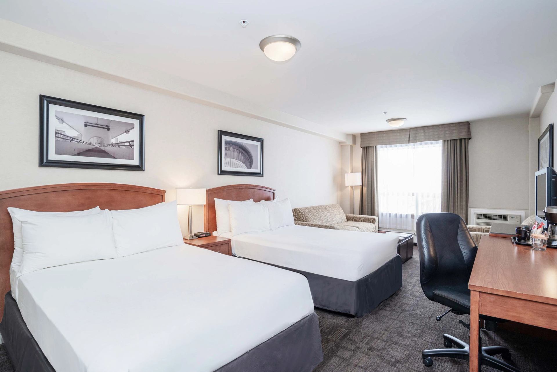 Hotel room with two beds, sofa, desk, office chair and window with curtains.