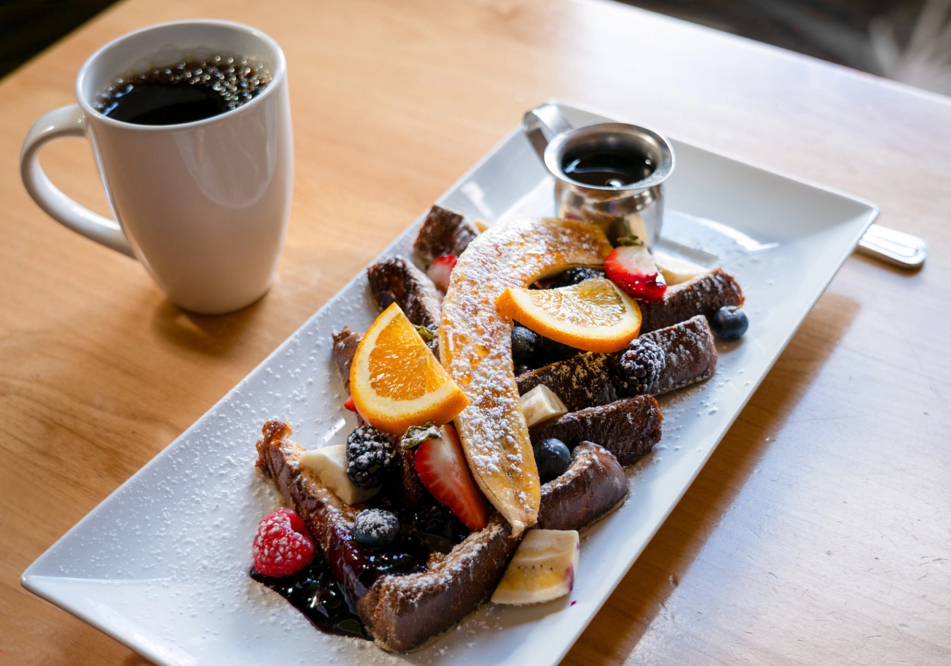 French toast with fruit and syrup beside coffee at Alpha Bistro.