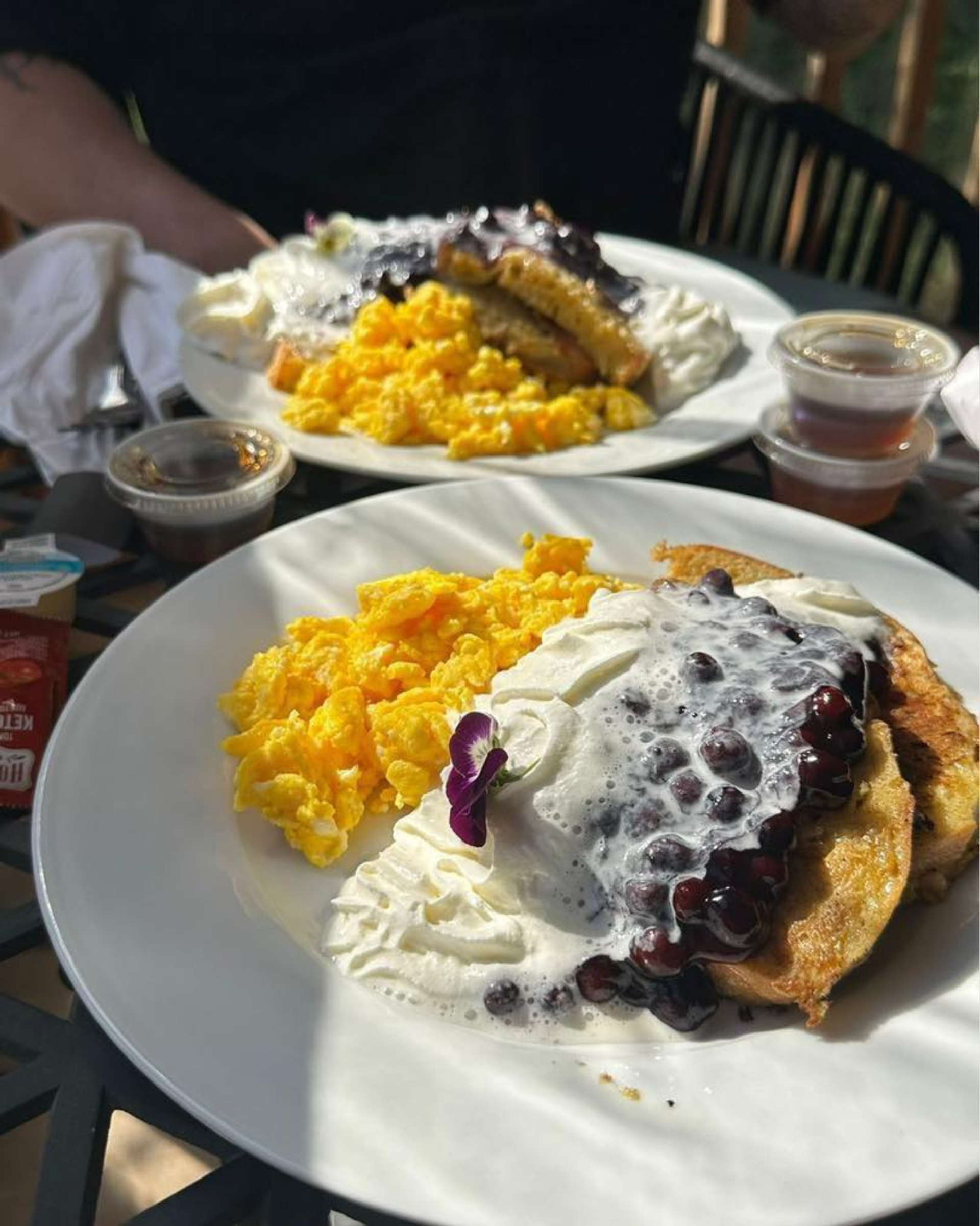 Breakfast plates with scrambled eggs, pancakes topped with whipped cream and blueberry sauce