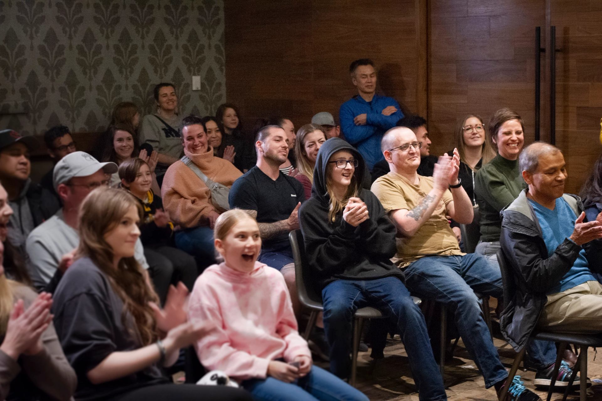 Seated audience members clapping inside a small venue during a live magic performance.
