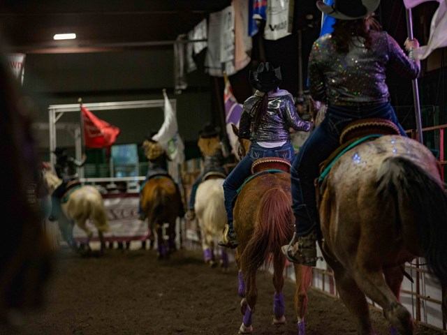 Mounted riders carrying flags as they move through a rodeo arena during an opening ceremony.