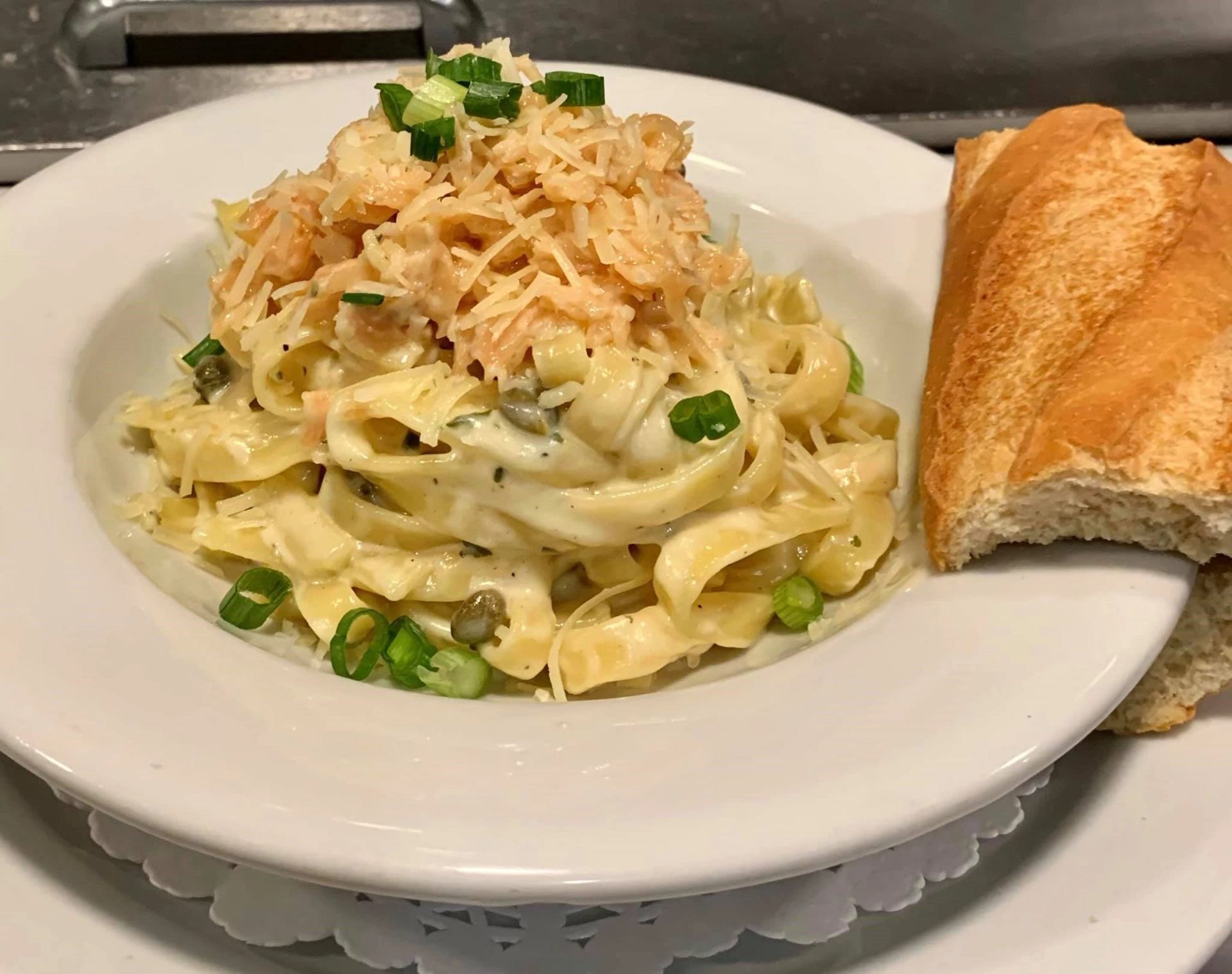 Fettuccine Alfredo topped with green onions and served with crusty bread in a white bowl.