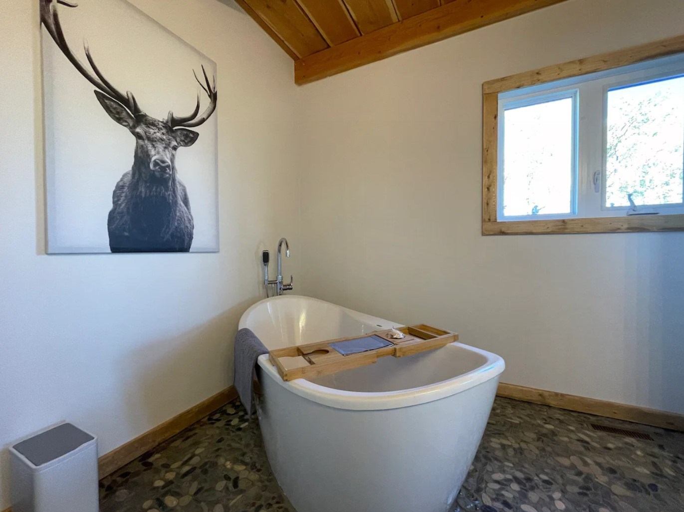 Freestanding tub with tray and deer art in cozy bathroom with window.