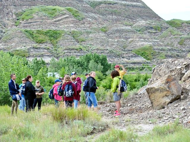 Tour group listening to guide near rocky outcrop and green hills