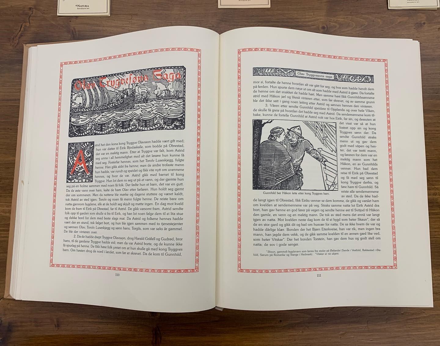 Open book with ornate illustrations and decorative red borders on both pages.