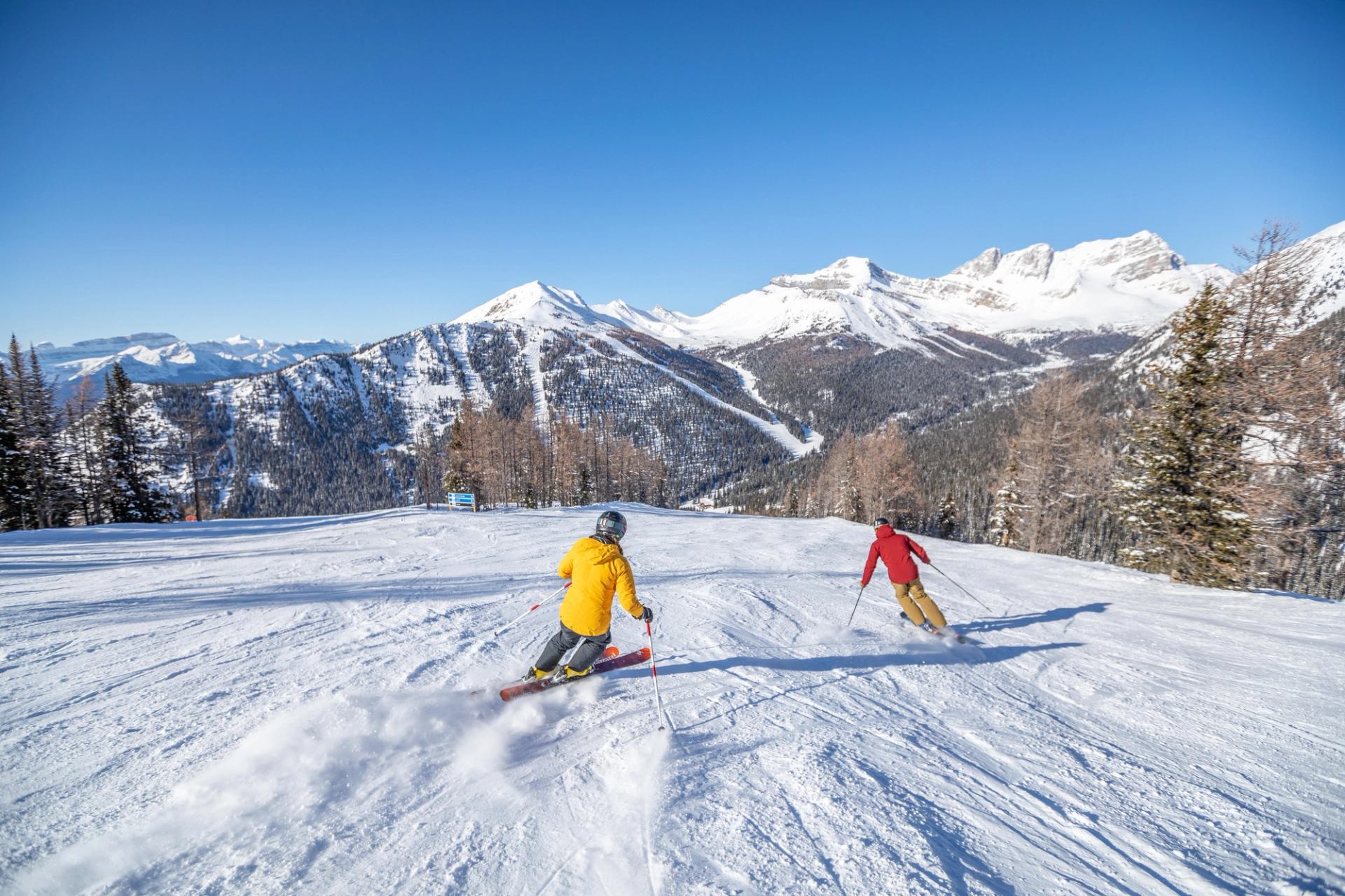 Two skiers on a snowy slope with mountain peaks in the background.