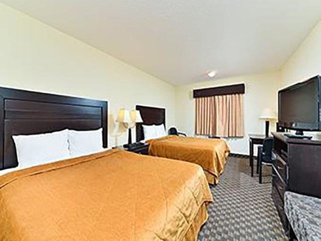 Hotel room with two beds, table lamps, window blinds, and flat-screen TVs.