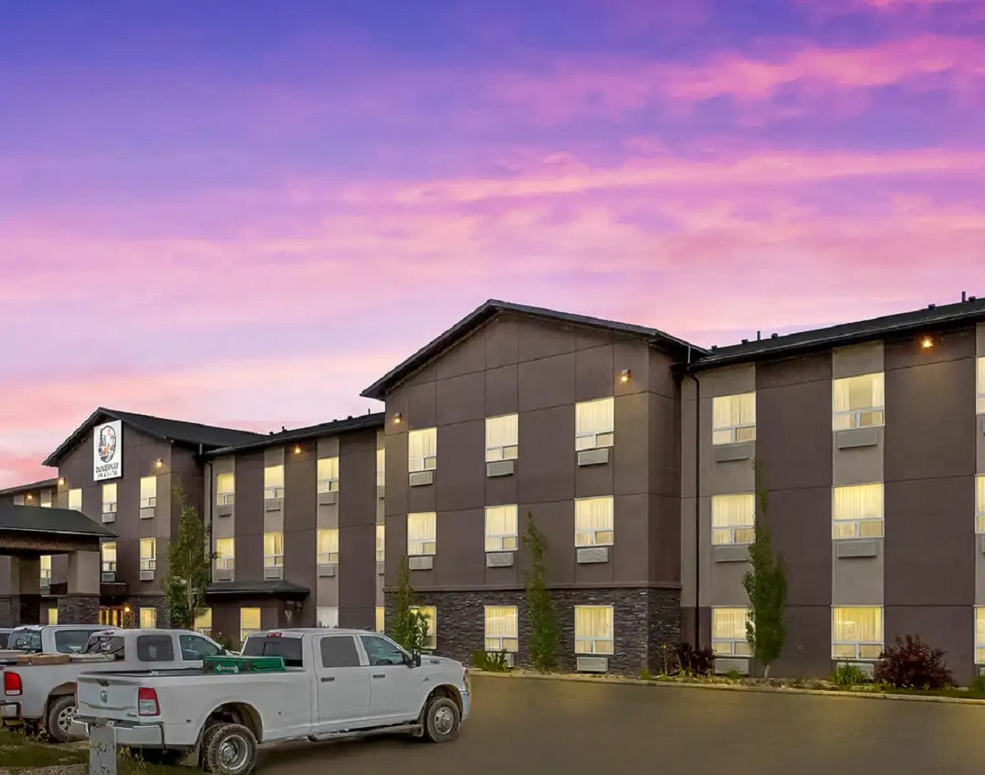 Modern hotel exterior at sunset with parked white trucks.