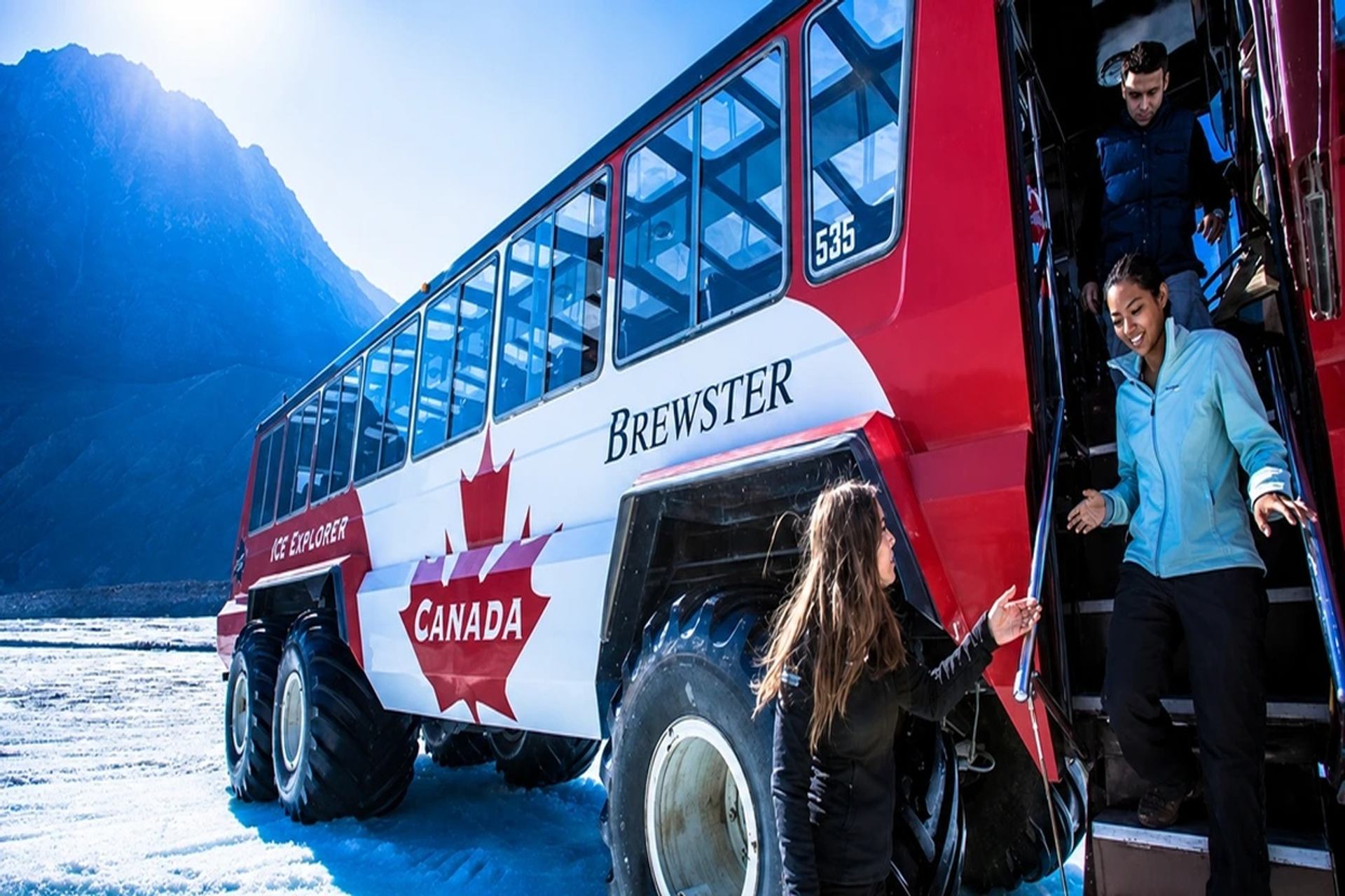 Passengers exit a red Brewster Ice Explorer bus beside a snowy mountain.