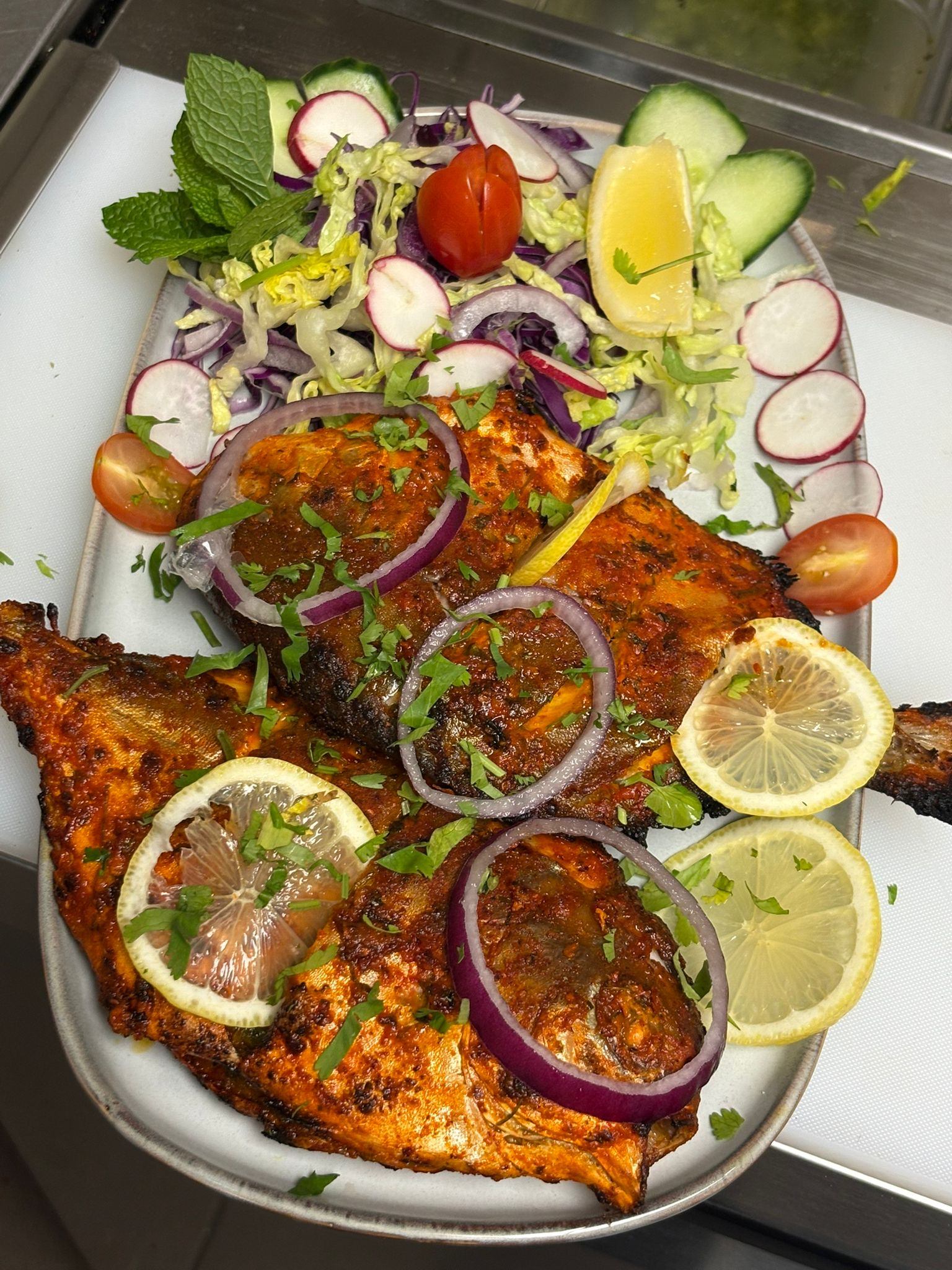 Grilled fish with salad, onions, lemon, and herbs on a vibrant plate.