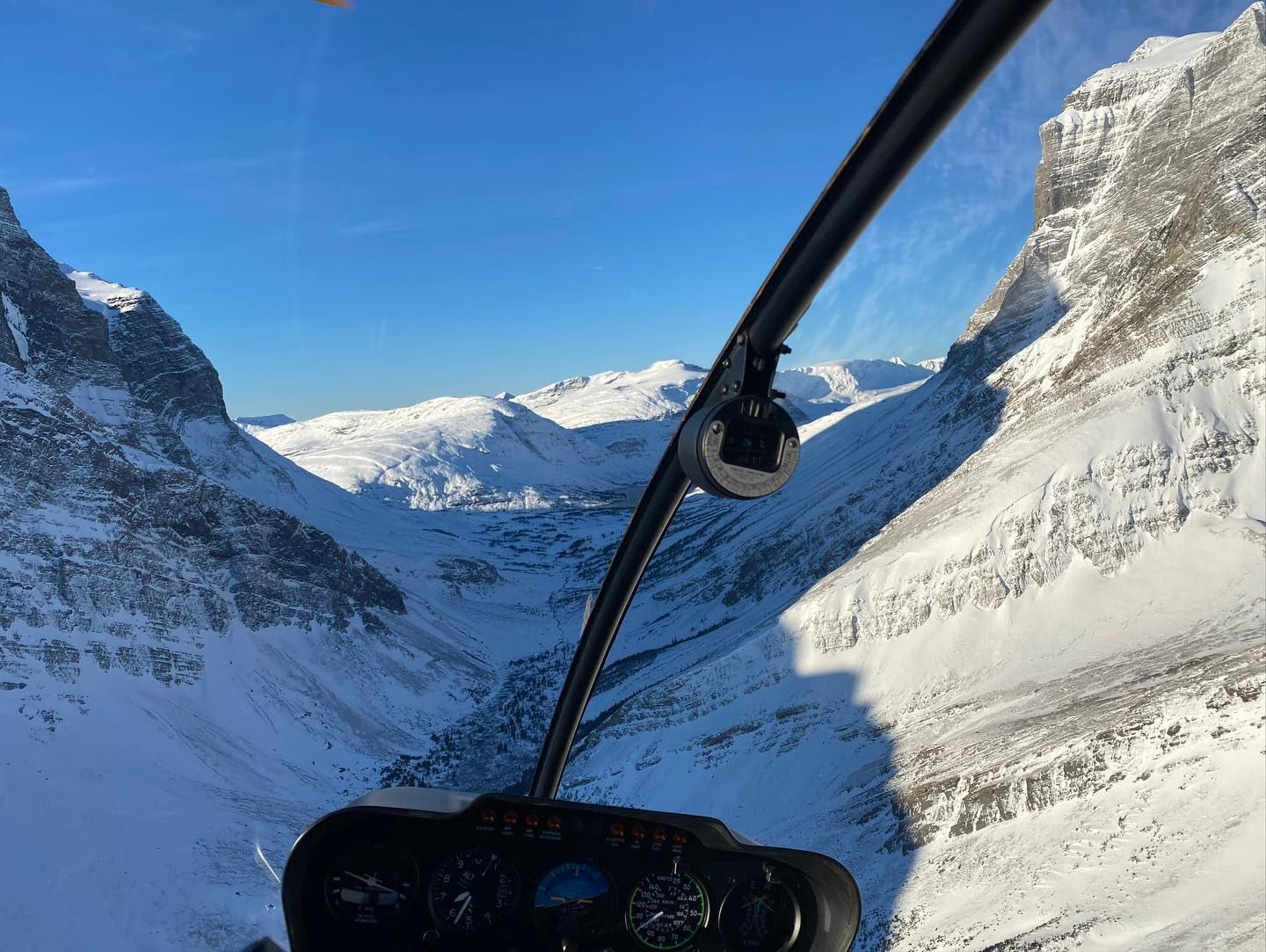 Cockpit view flying over snowy mountains under clear blue sky.